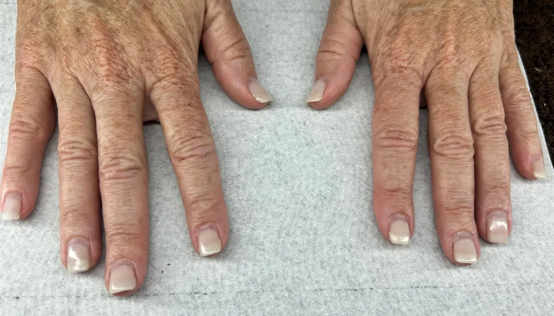 Two hands with polished, light-colored nails on a white surface.
