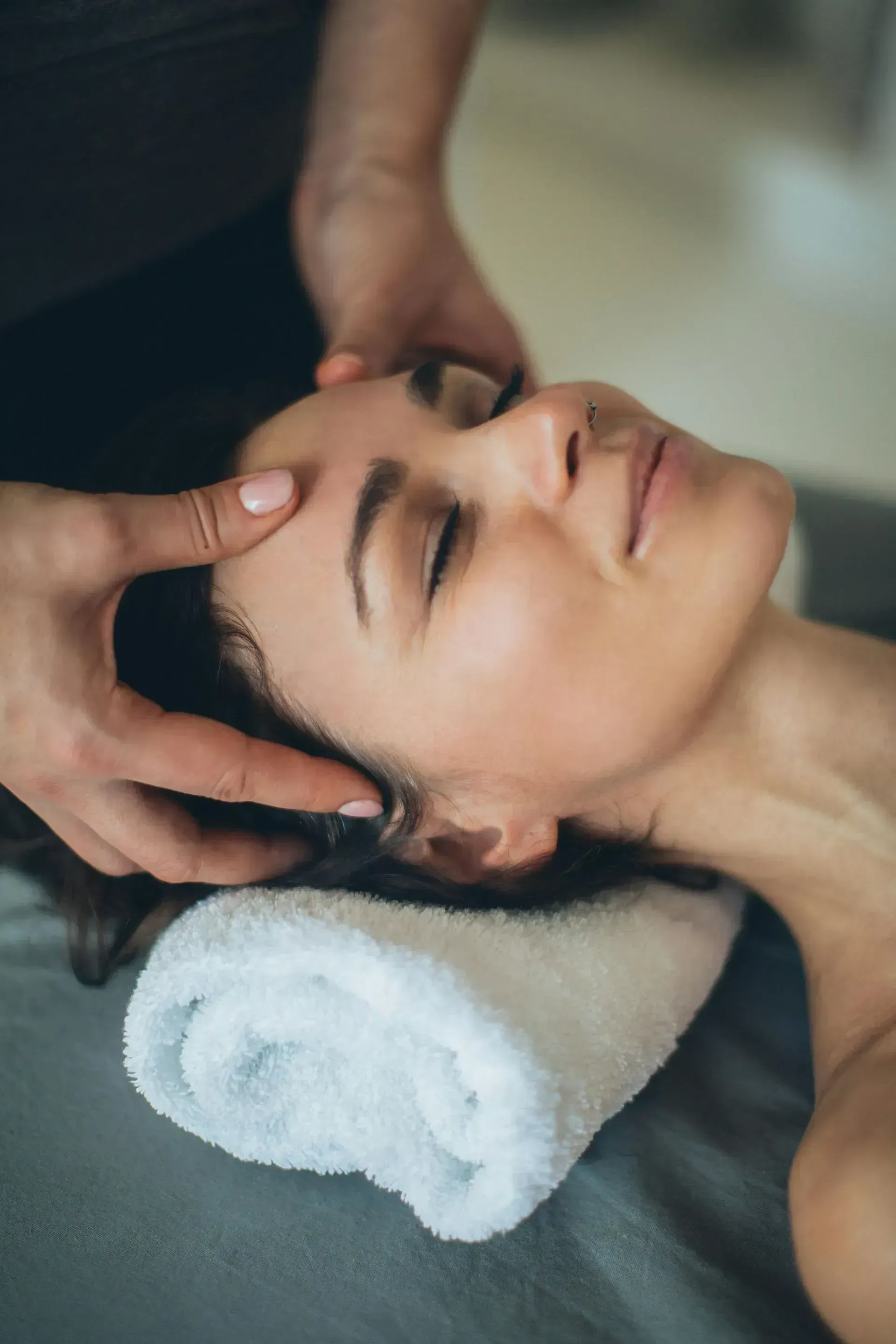 Woman receiving a head massage, eyes closed, on a massage table with a white towel.