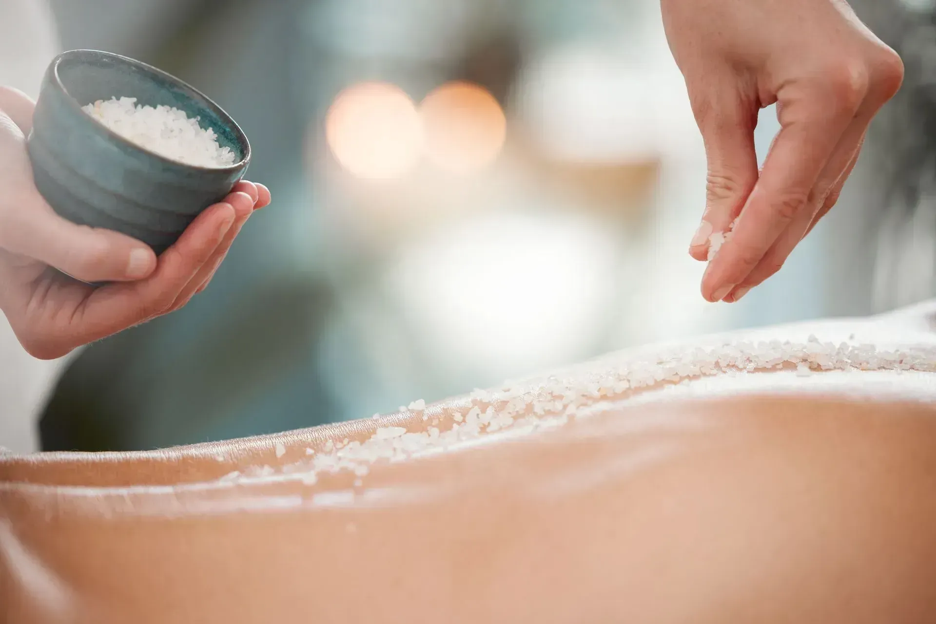 Person receiving salt scrub treatment on their back; hands pouring salt.