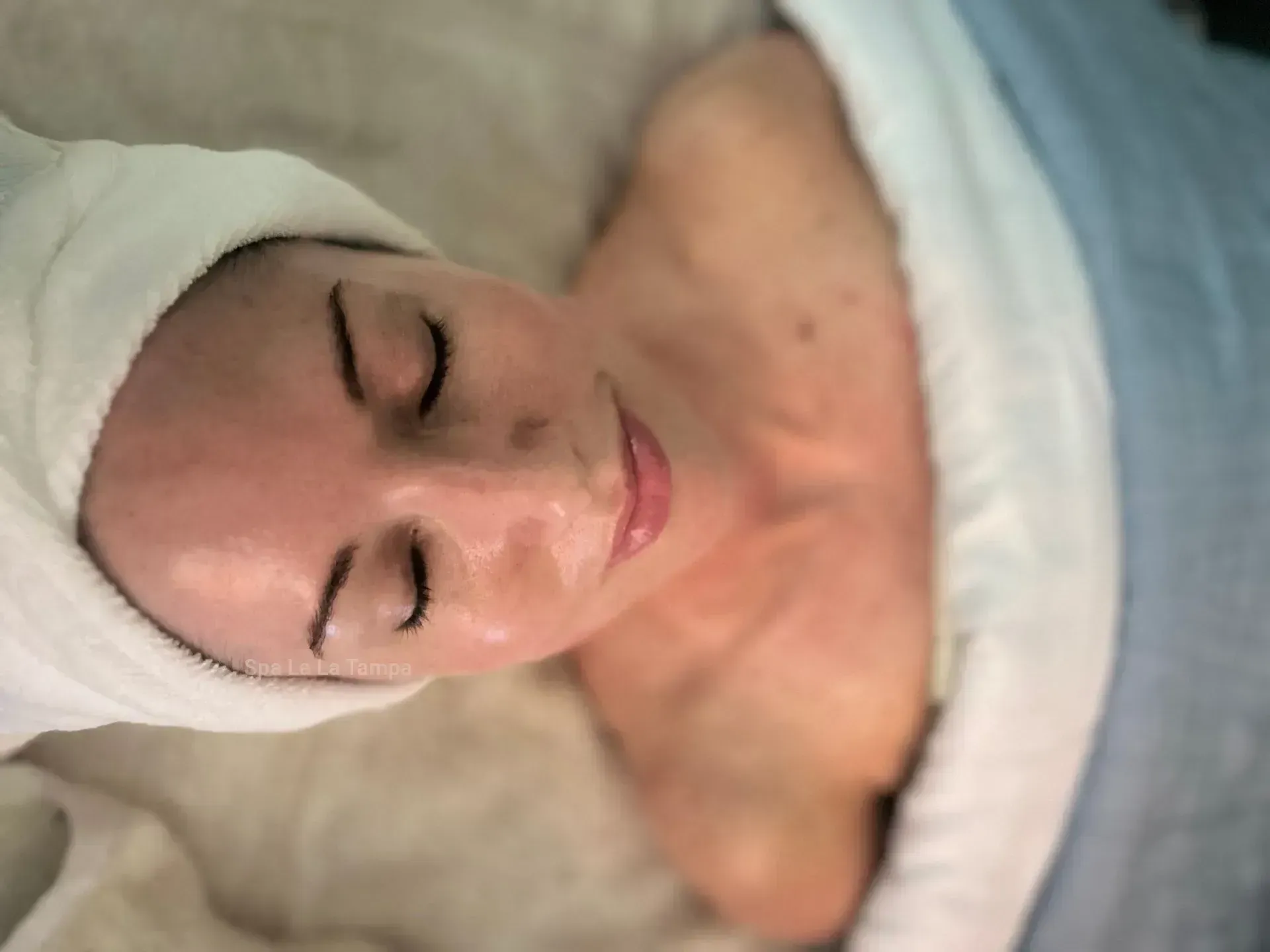 Woman with eyes closed, wrapped in a towel, receiving a facial.