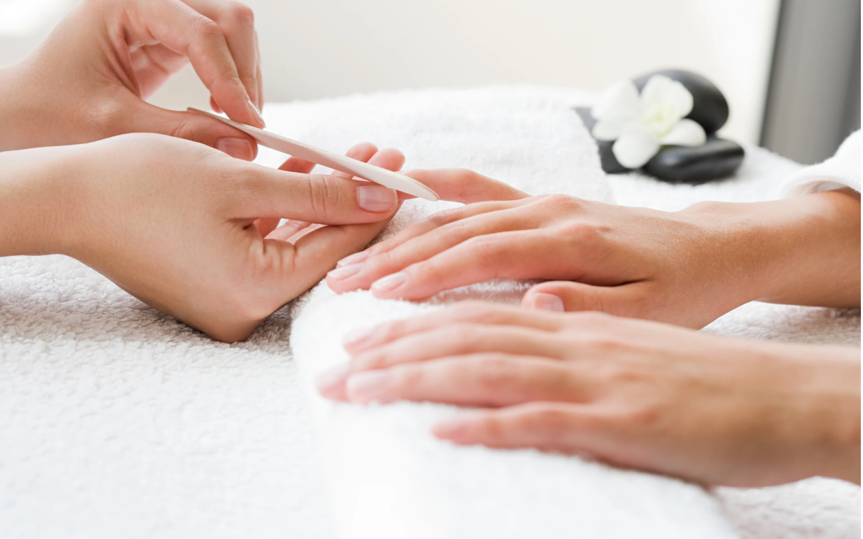 Manicurist filing a person's fingernails, hands resting on a white towel.