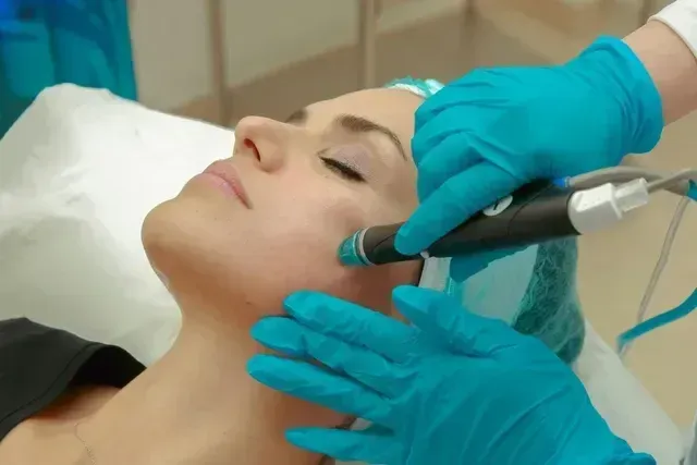 Gloved clinician using HydraFacial handpiece on the client's cheek