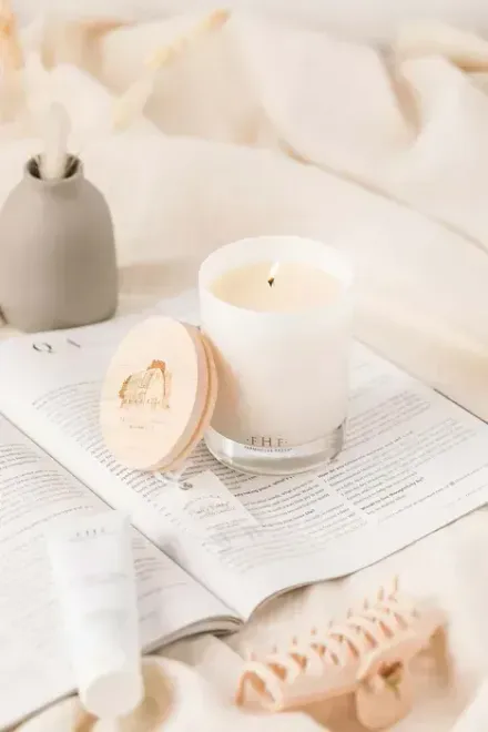 White candle burning on a newspaper with a wooden lid, small vase, and hair clip.