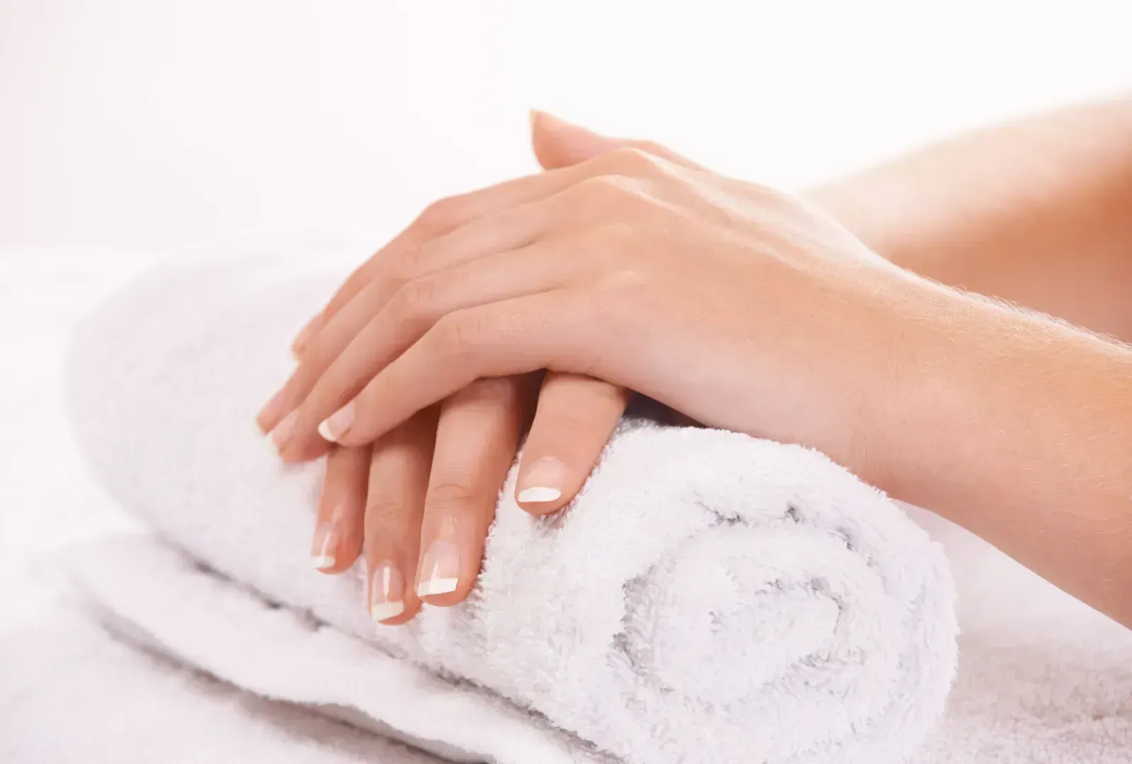 Hands with French manicured nails resting on a rolled white towel.
