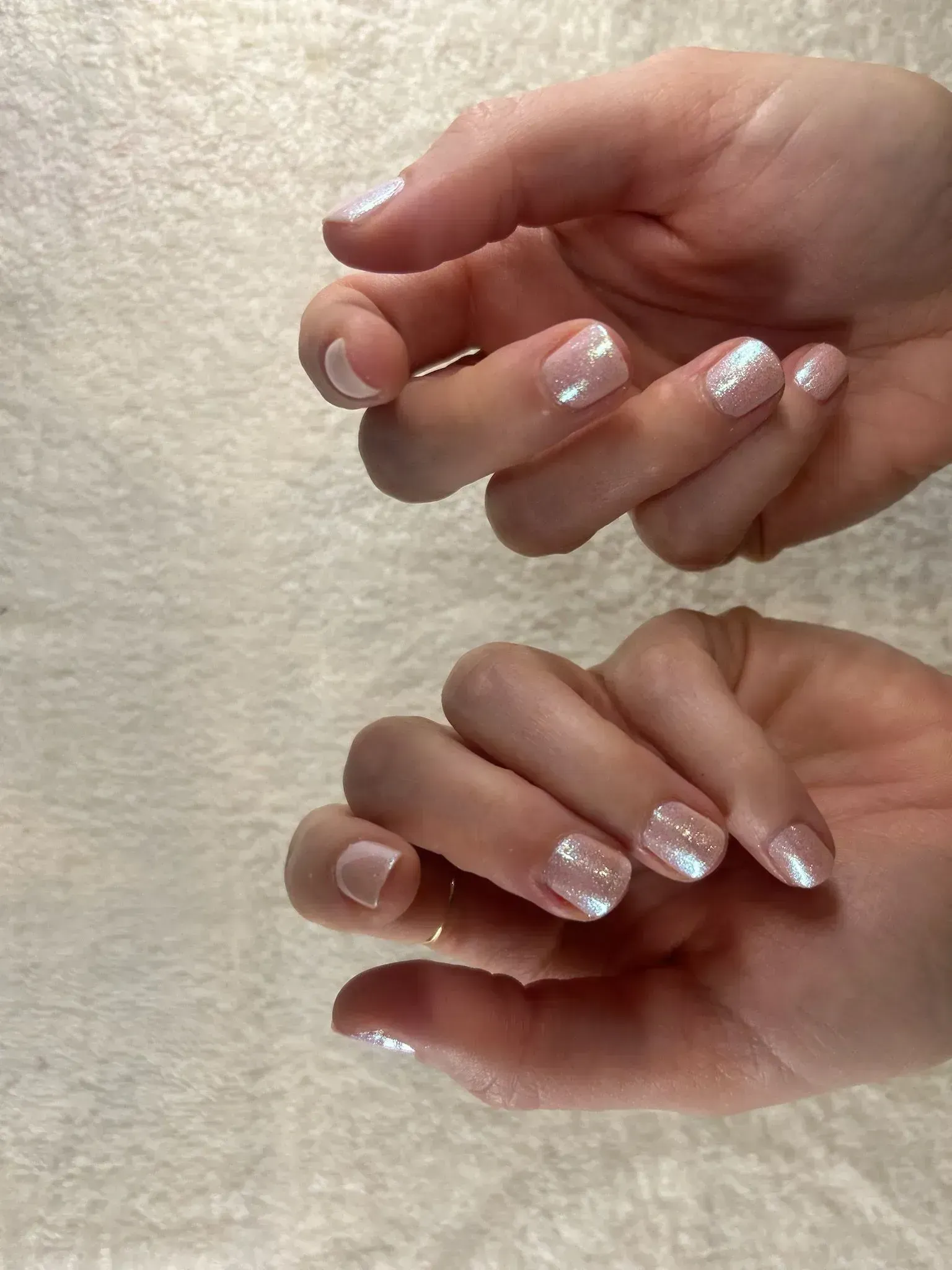 Hands with light pink and white iridescent nail polish on a soft white towel.