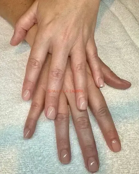 Two hands with nude-colored nail polish, resting on a white surface.