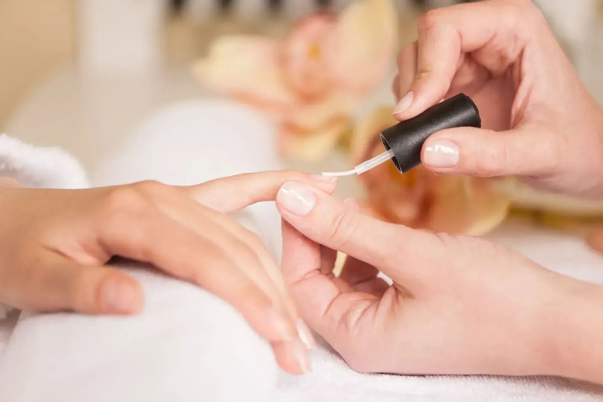 Manicurist applying clear nail polish to a client's fingernail at a salon.