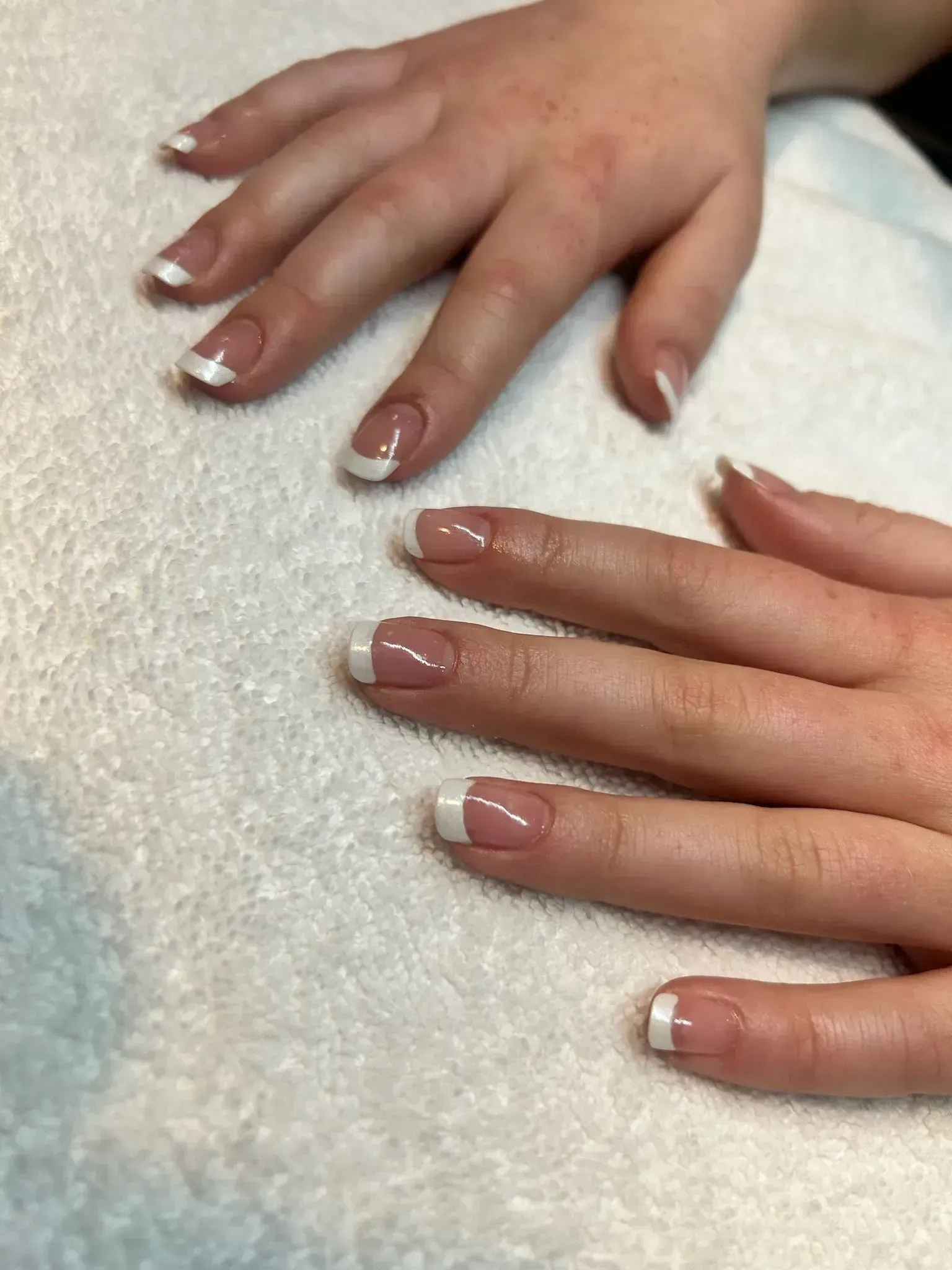 Hands with French tip manicured nails resting on a white towel.