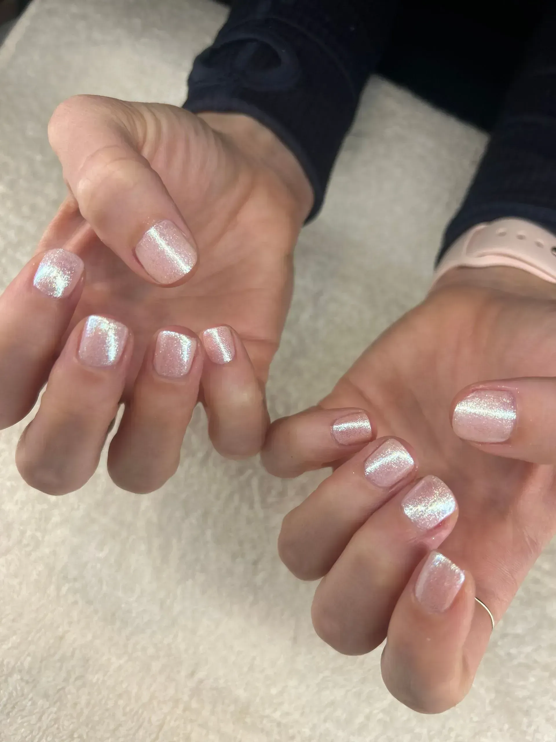 Hands with light pink and sparkly square nails, resting on a white surface.