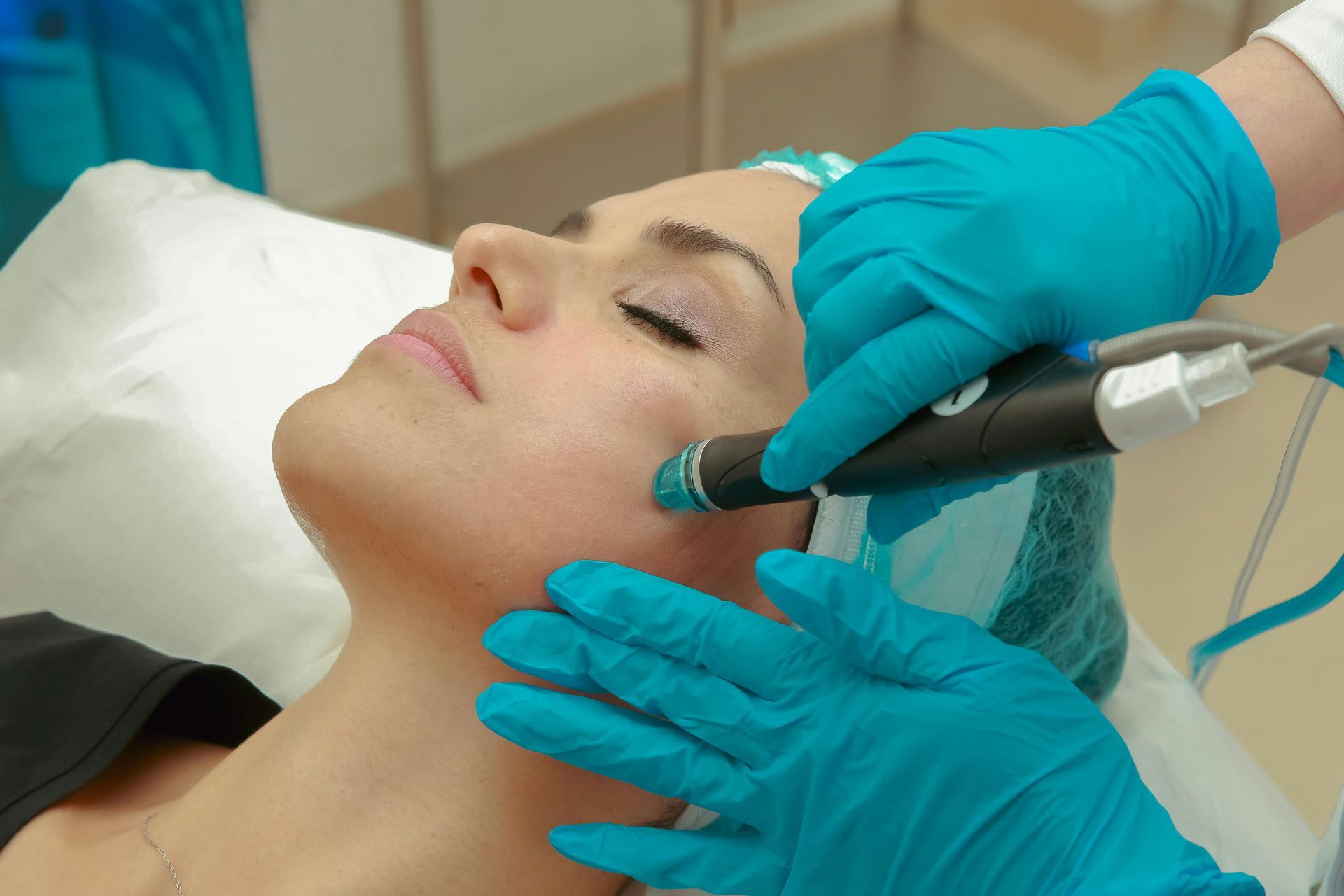 Woman receiving hydrafacial treatment, smiling, lying on white bed, esthetician holding device.