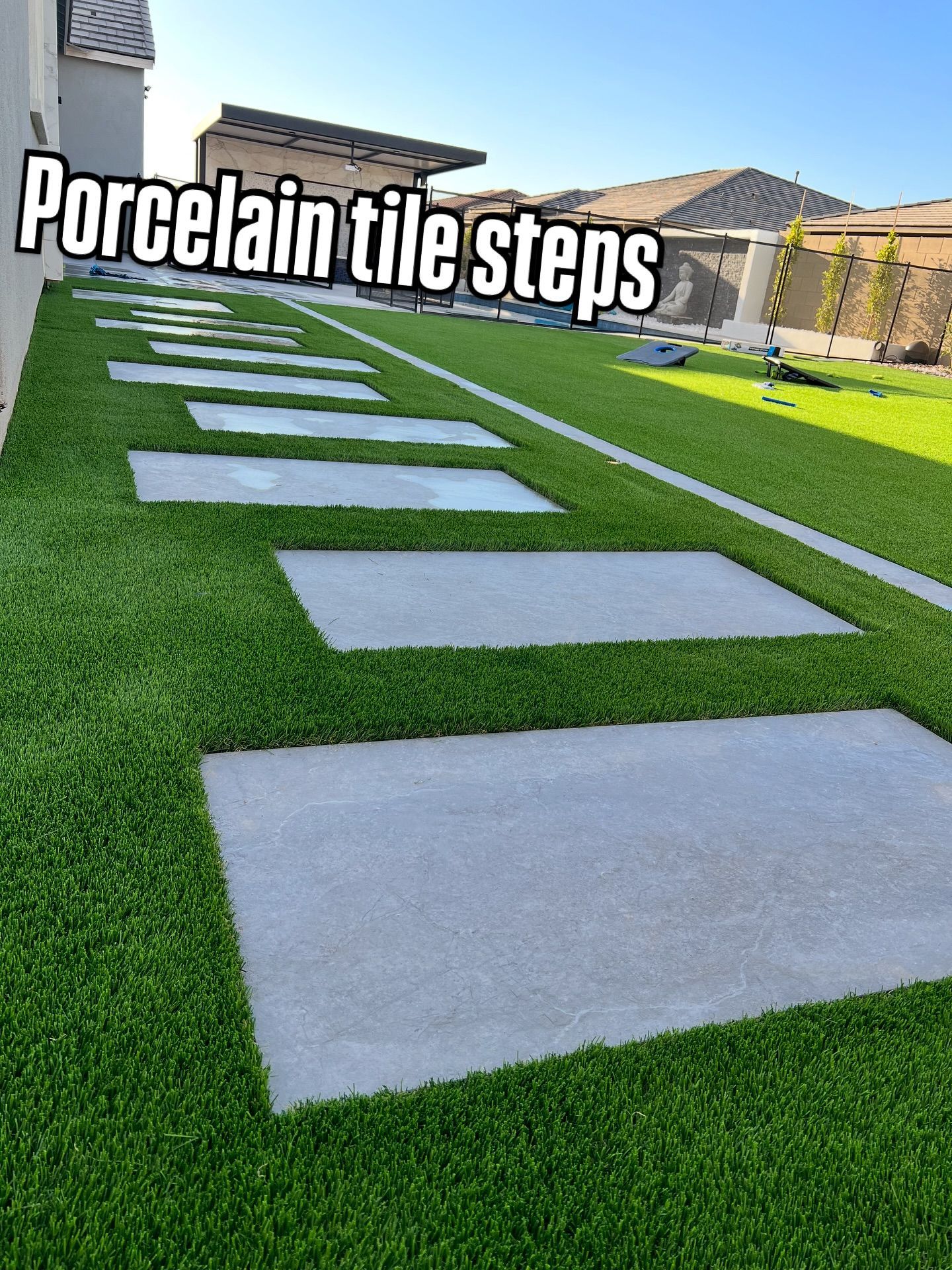 Rectangular gray porcelain tile pavers set into a vibrant green artificial grass lawn in a residential backyard.