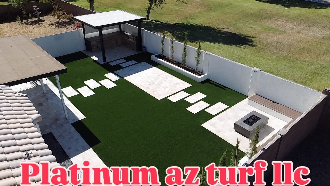 A landscaped backyard features artificial turf, stone pavers, a gazebo, a fire pit, and a planter wall.