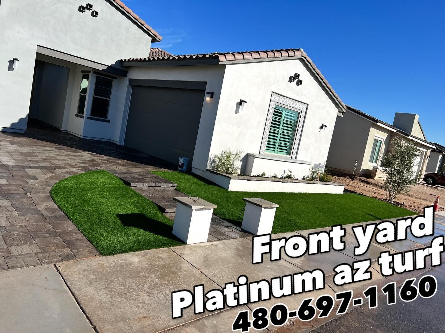 A residential front yard featuring neatly installed synthetic turf, a paved walkway, and a modern stucco home exterior.