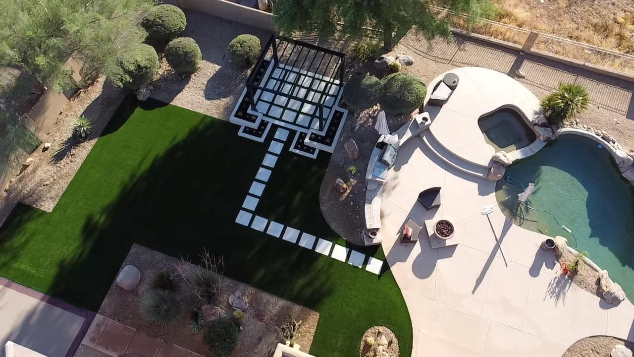 Aerial view of a backyard with a pool, spa, pergola, paver patio, and lawn area.