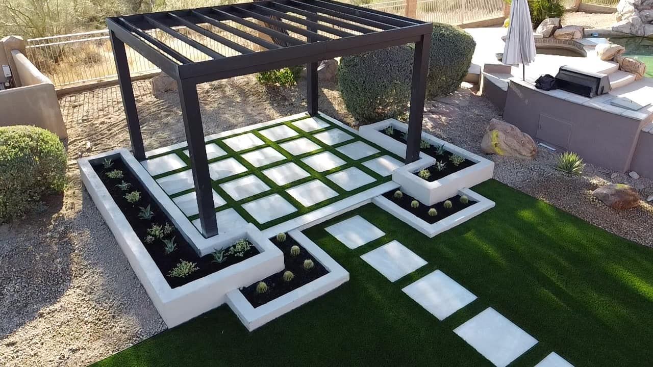 A modern wooden pergola over a square paver patio with artificial grass, surrounded by tiered concrete planters.