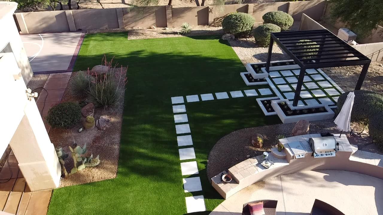 An aerial view of a modern backyard featuring artificial grass, a stone paver path, a pergola, and a curved patio area.