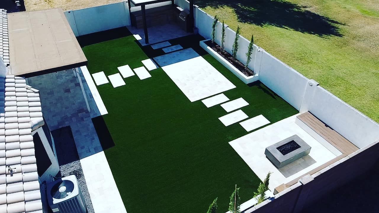 An aerial view of a modern backyard with a green lawn, concrete stepping stones, a fire pit, and a small gazebo.