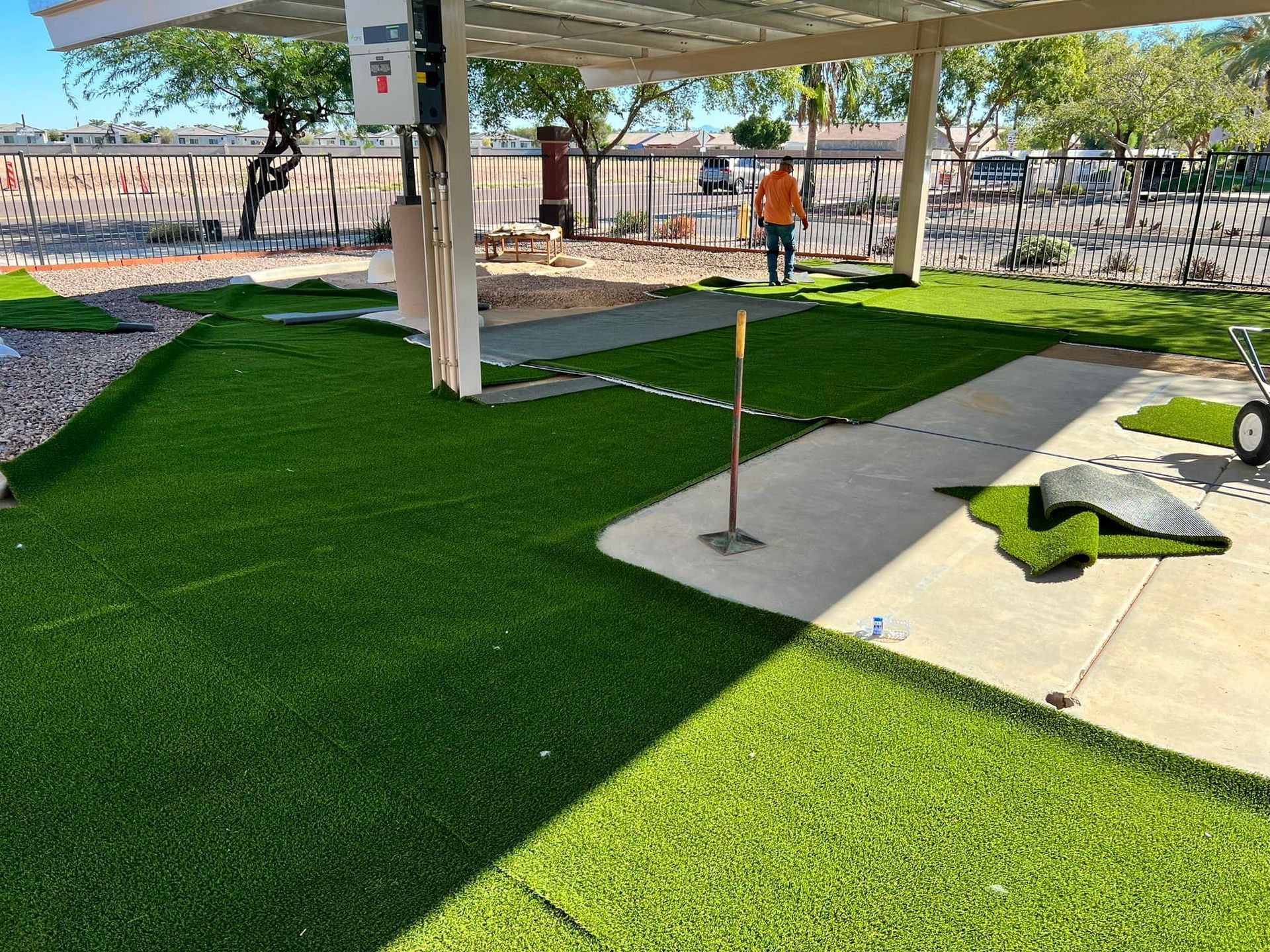 A person wearing an orange shirt walks across a grassy area partially covered by a metal patio roof.