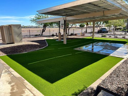 A solar panel carport shading an area of artificial grass with a concrete pad and gravel landscaping.