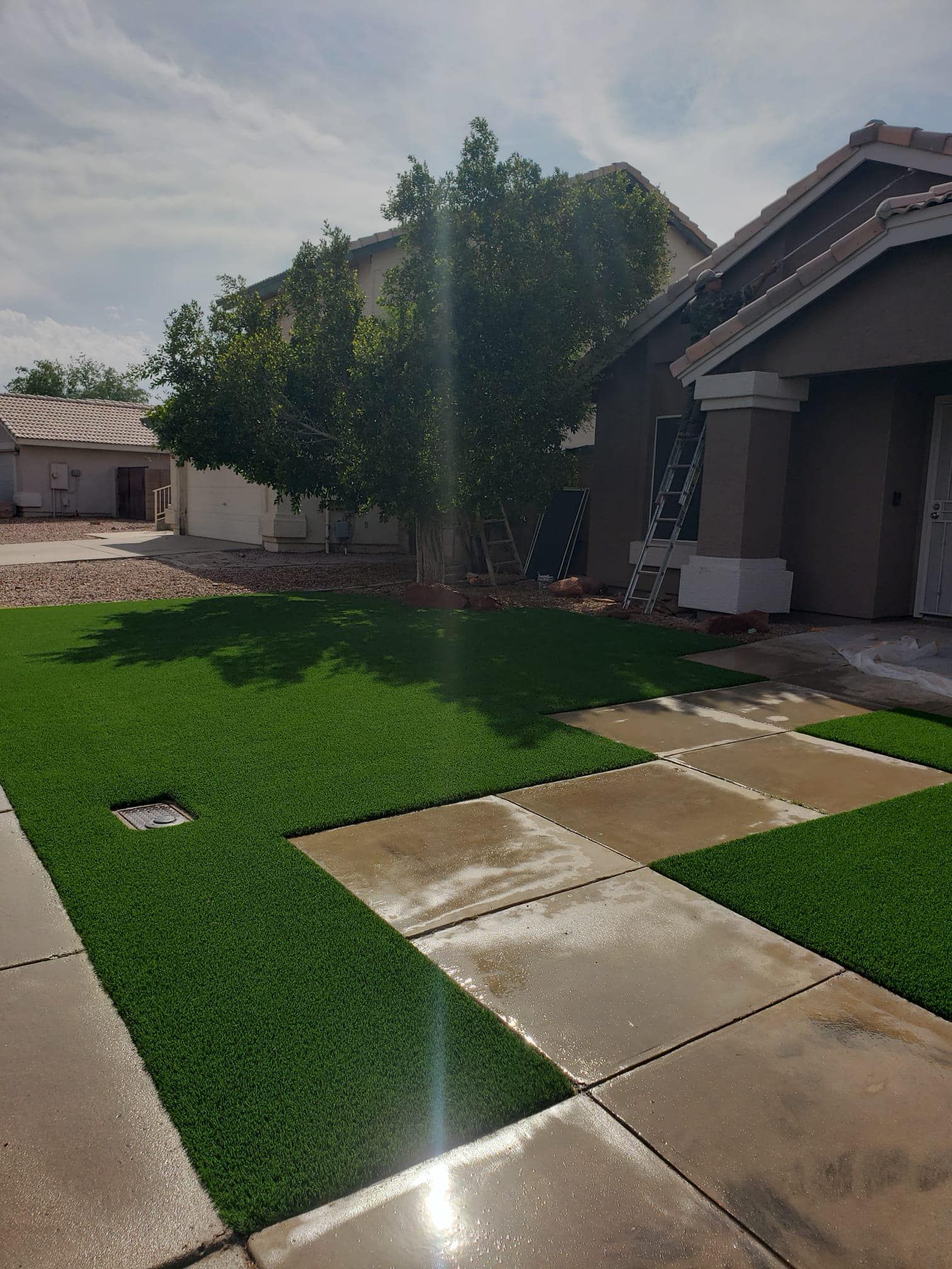 A modern front yard featuring green synthetic grass patches bordered by large, gray concrete pavers next to a house.