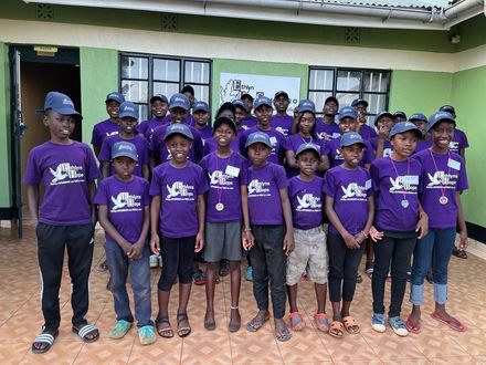 a group of children wearing purple shirts and hats are posing for a picture .