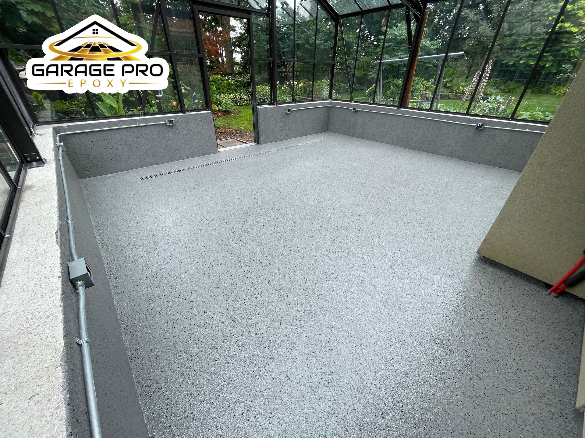 A garage with a concrete floor and a greenhouse in the background.