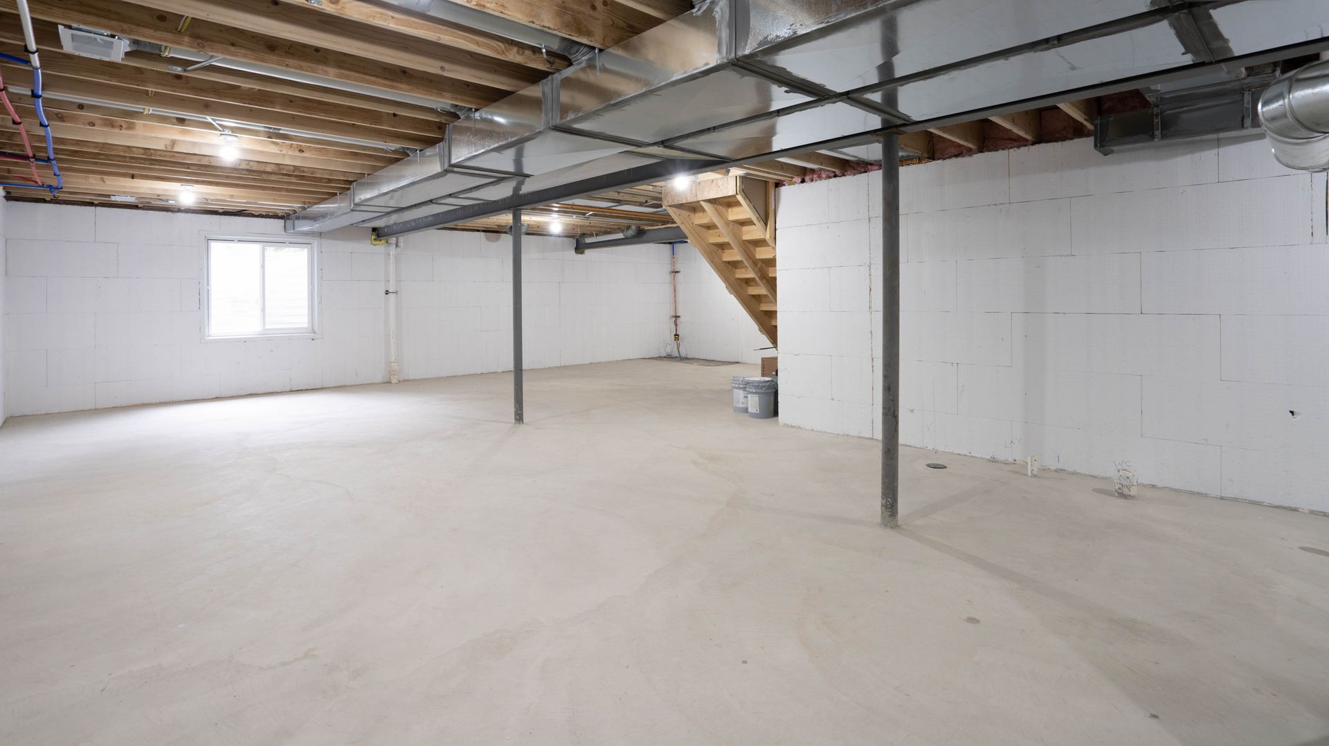 An empty basement with white walls and a wooden staircase.