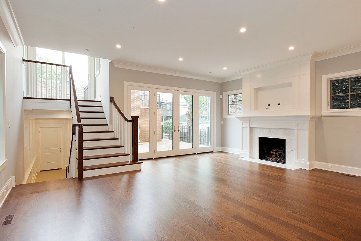 An empty living room with hardwood floors , stairs and a fireplace.