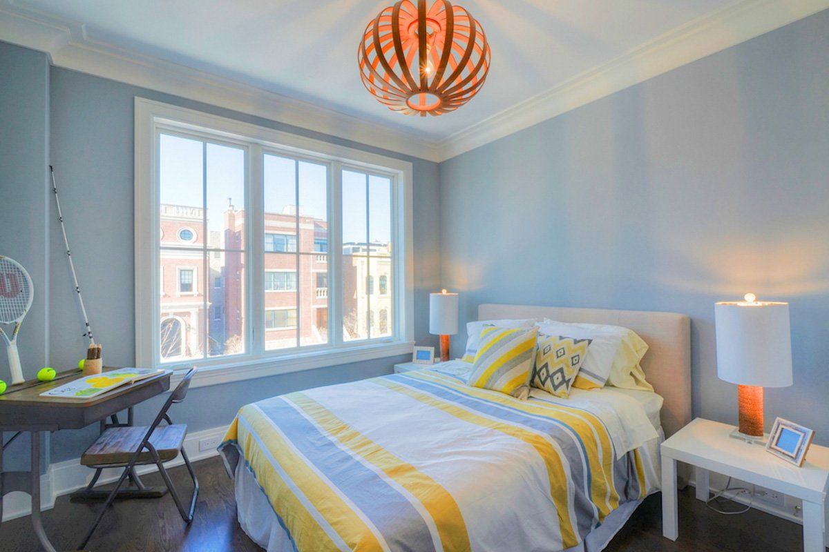 A bedroom with a bed , desk , lamps and a large window.