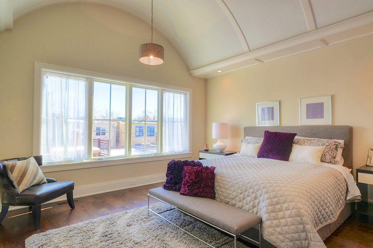A bedroom with a king size bed , a bench , a chair and a large window.