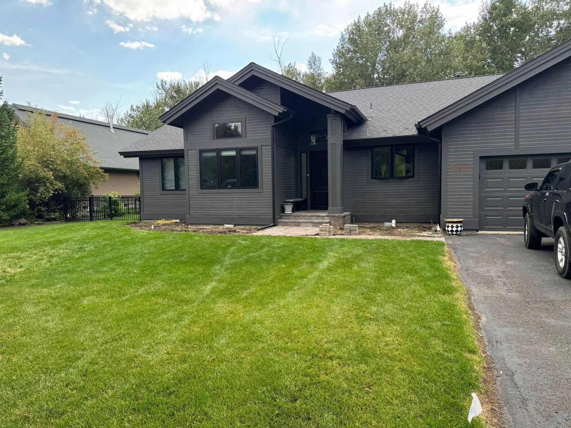 Dark gray house with green lawn, driveway, and parked car on a cloudy day.