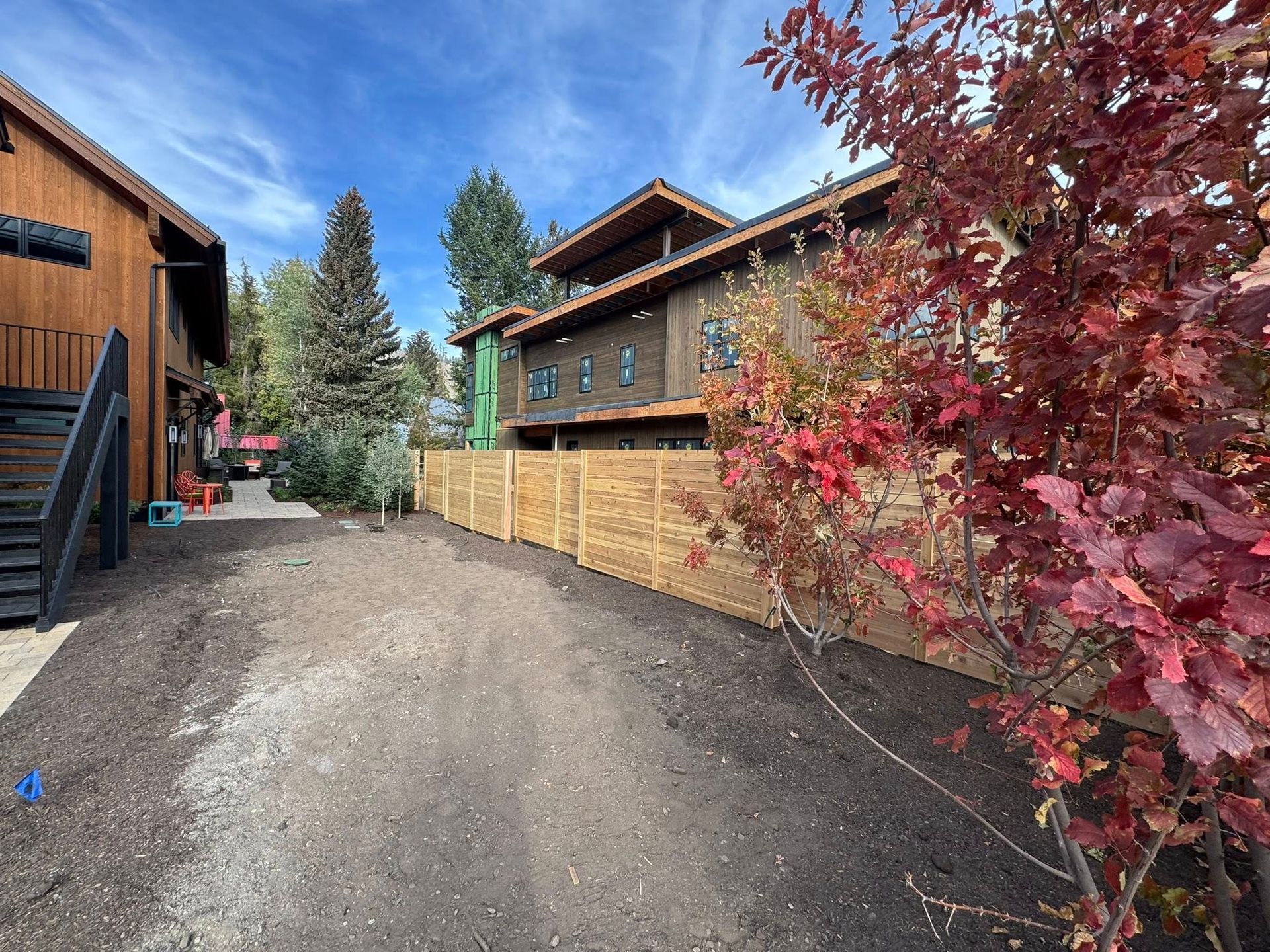 Dirt path between buildings, wooden fence, fall foliage. Blue sky.