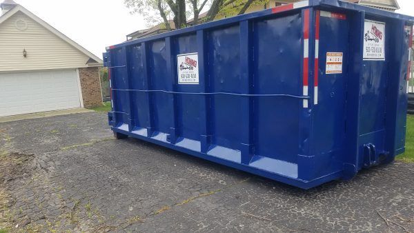 Blue dumpster in a driveway near a garage, for waste disposal.