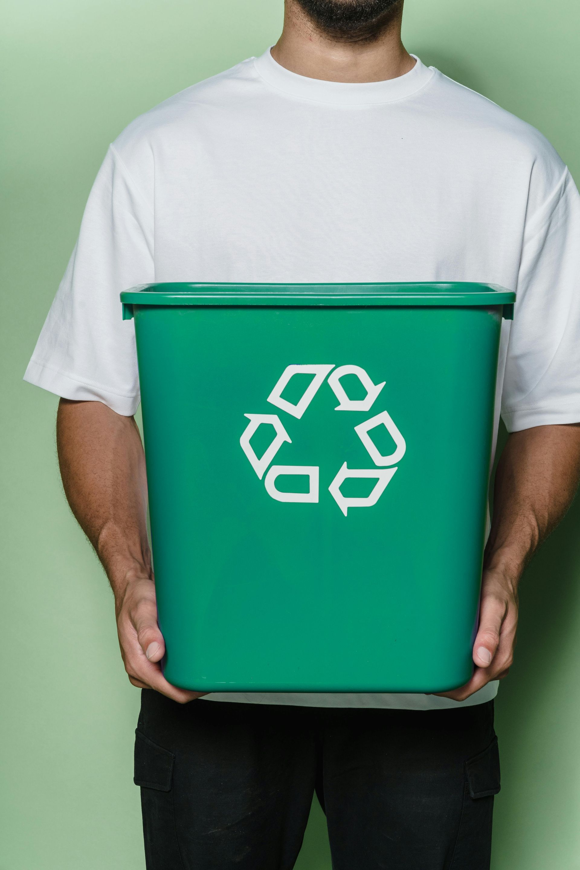 Person holding a green recycling bin with the recycling symbol on the front.