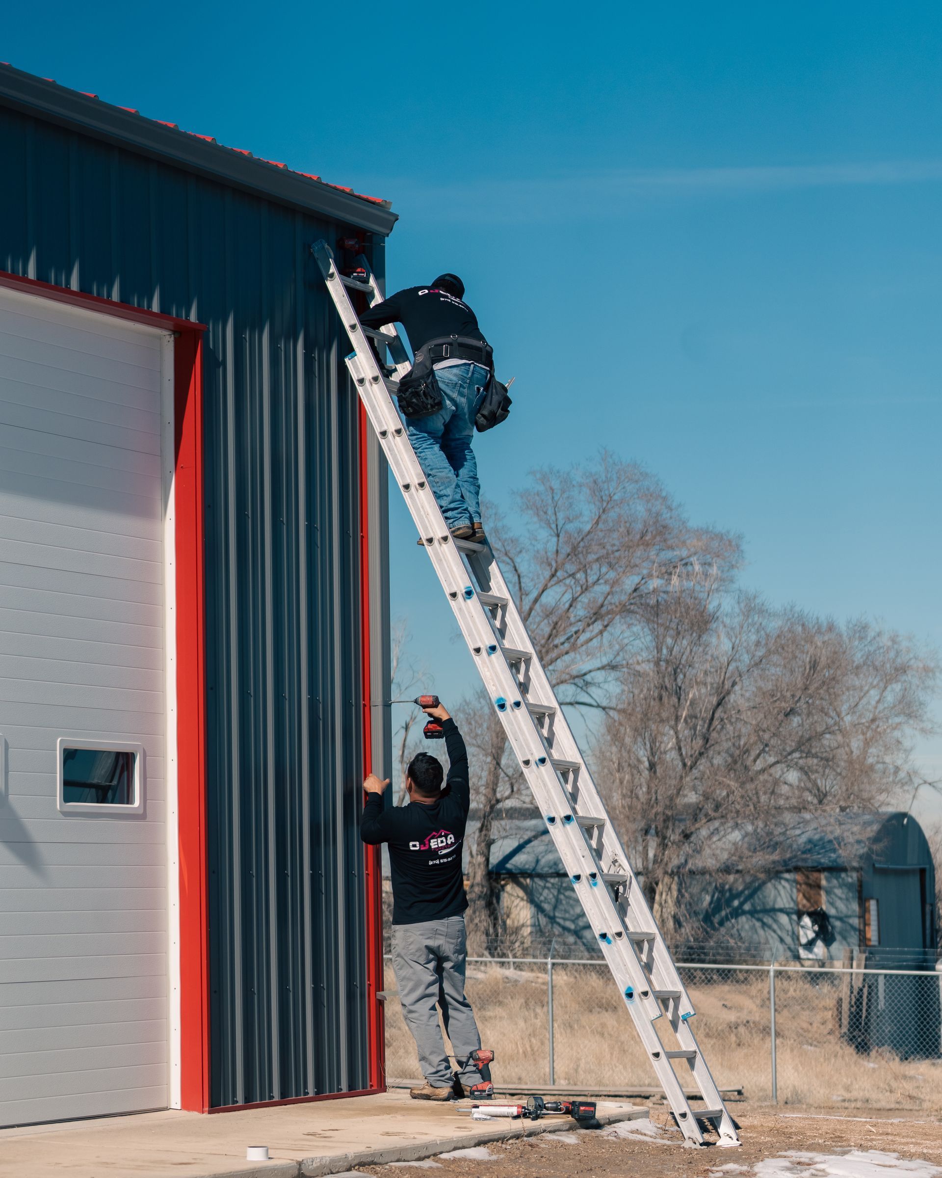 Two men are painting a building with a ladder.