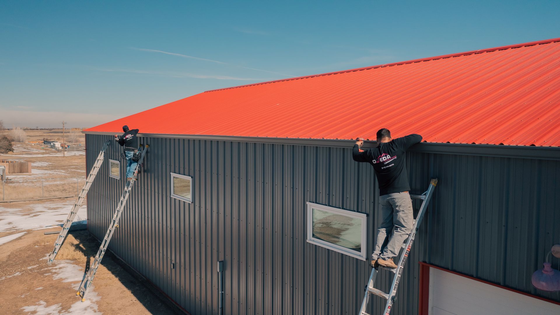 A man on a ladder is installing gutters on a building.