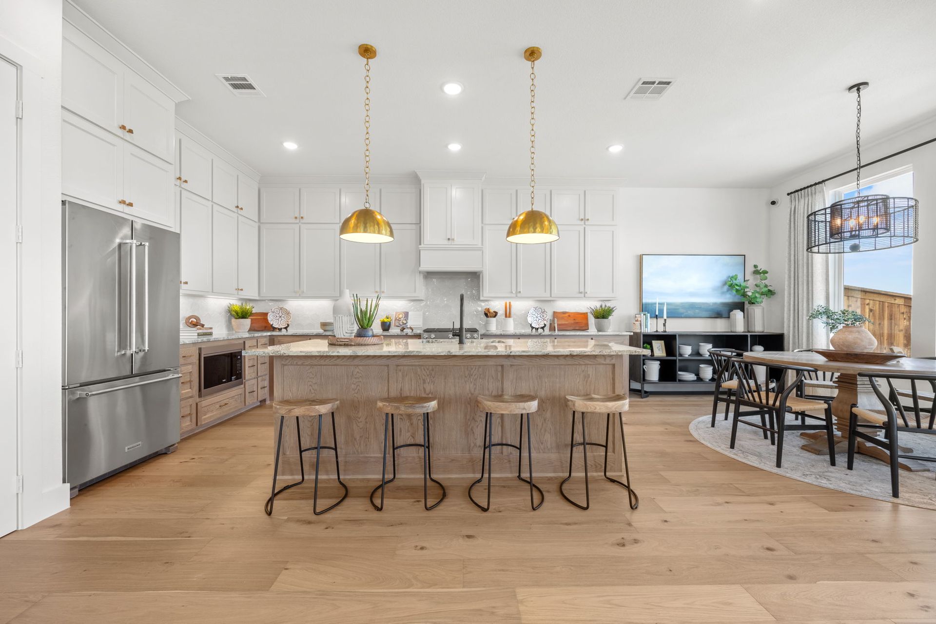 Modern kitchen with stainless steel appliances, island, light wood floors, and dining area.