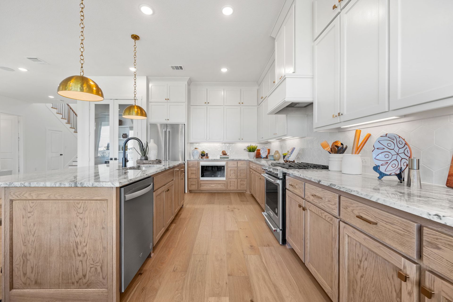 Bright kitchen with white and light wood cabinets, stainless steel appliances, and gold light fixtures.