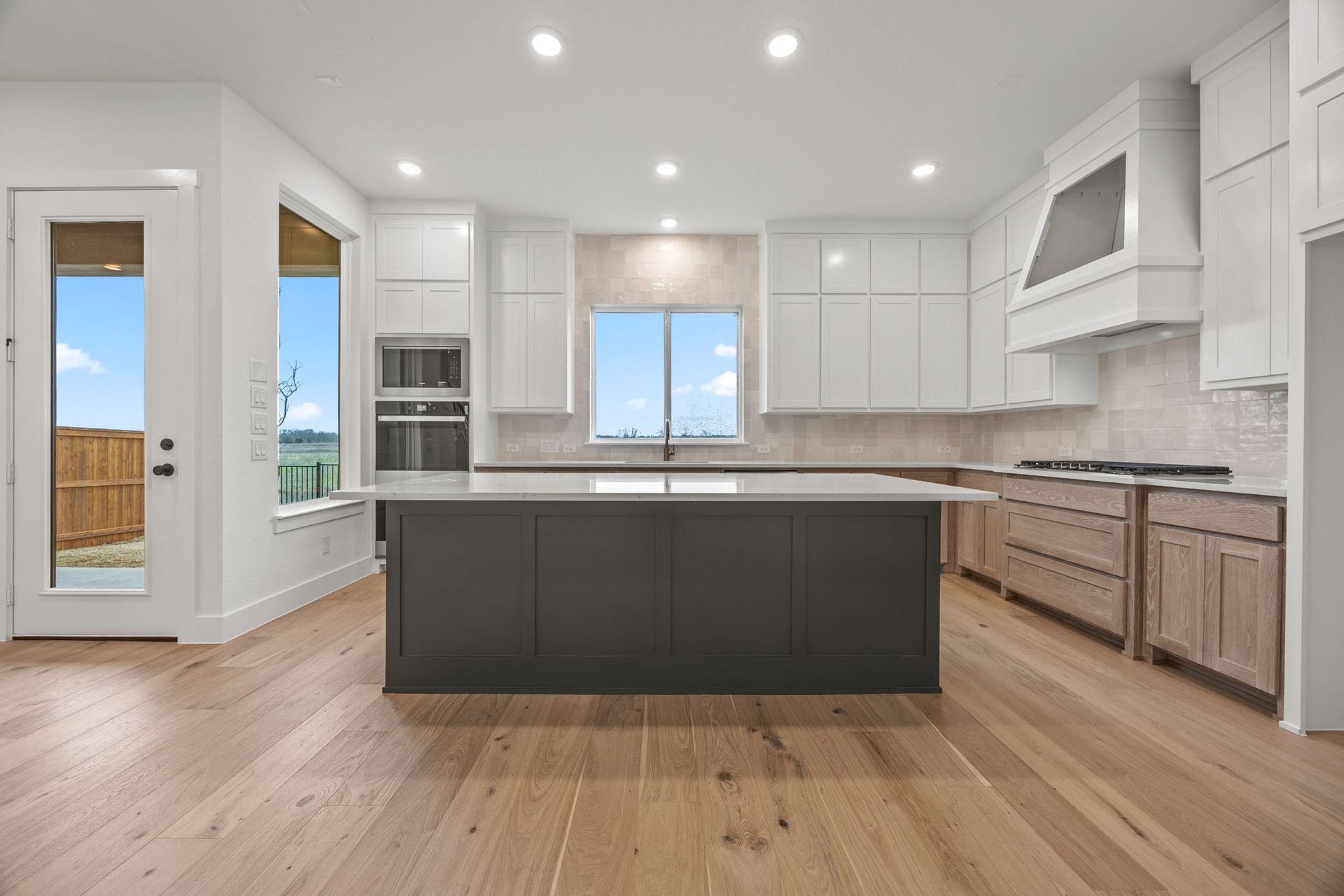 Modern kitchen with white and dark cabinets, island, and light wood floors; bright windows and a view.
