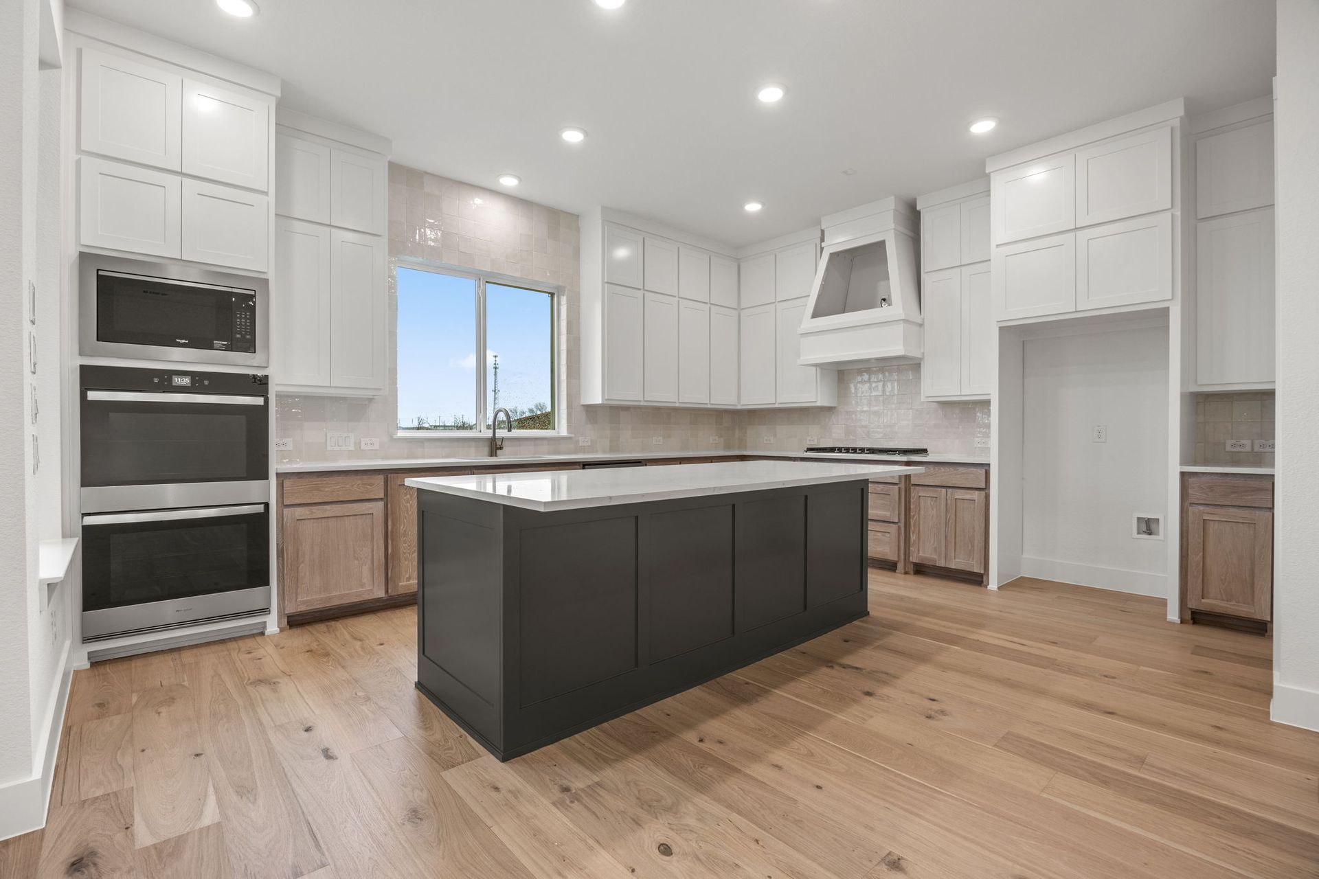 Modern kitchen with white cabinets, gray island, and wood floors.
