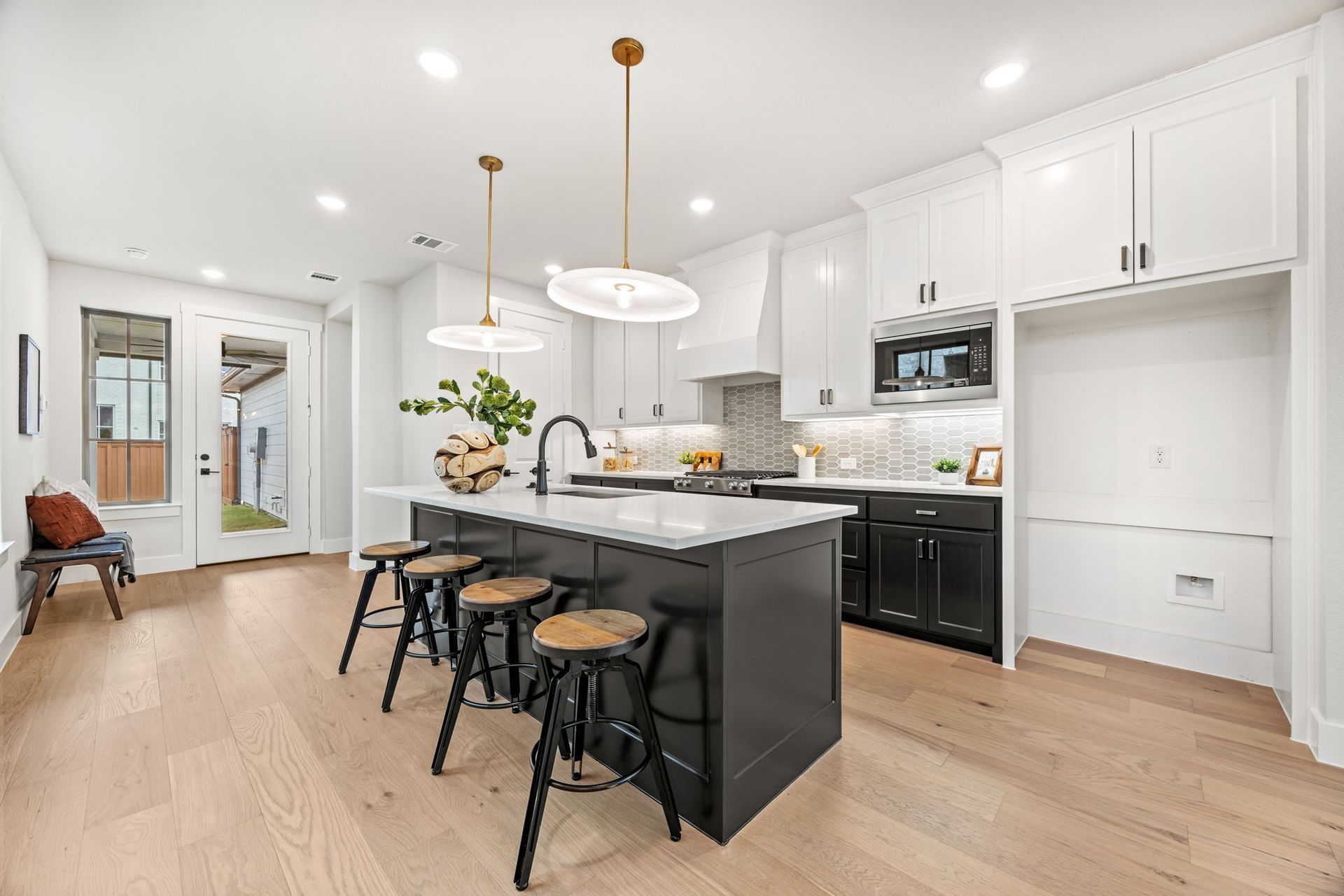 Modern kitchen with a black island, white cabinets, and light wood floors.