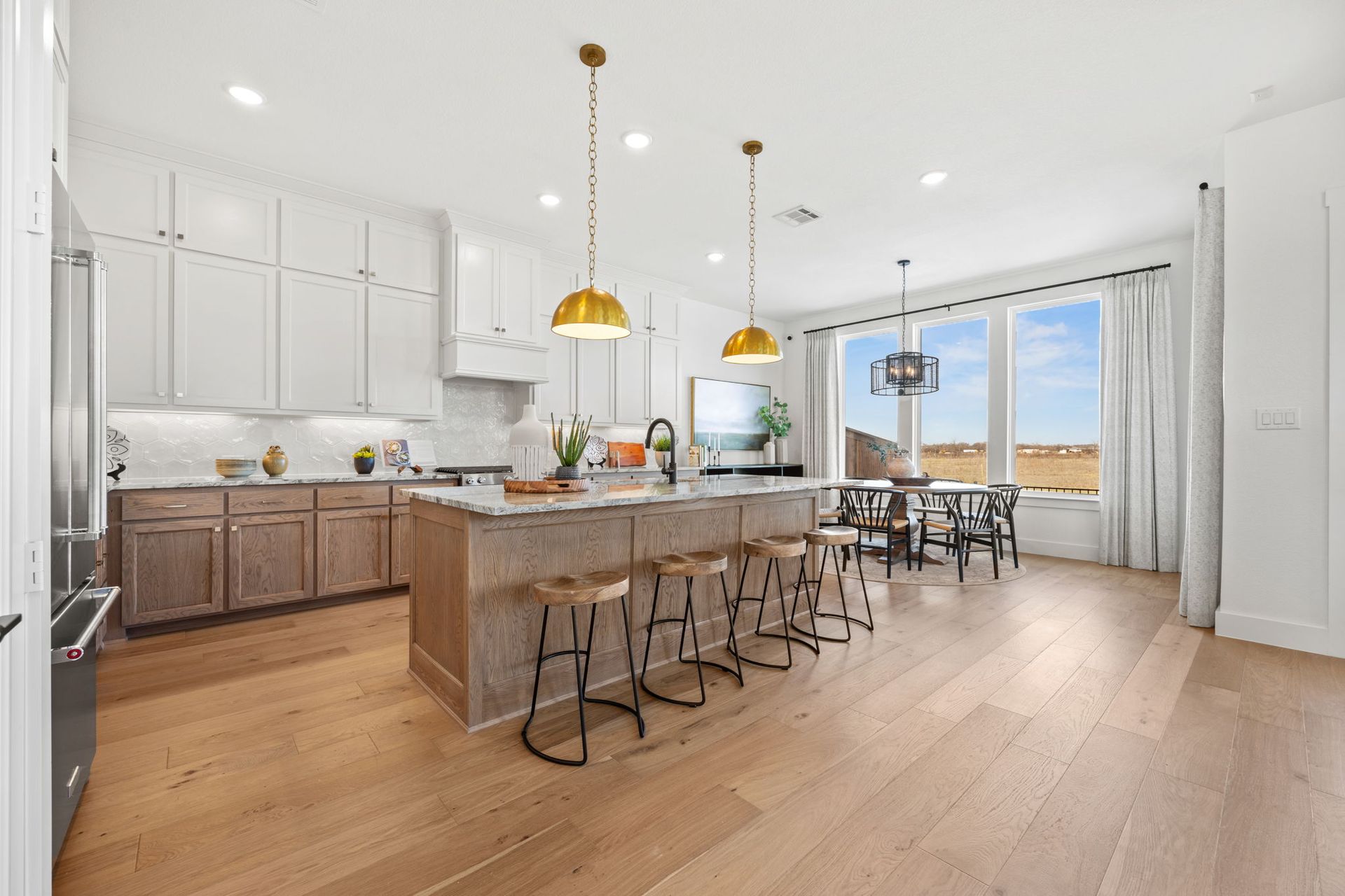 Modern kitchen with light wood cabinets, island with stools, and dining area with a view.
