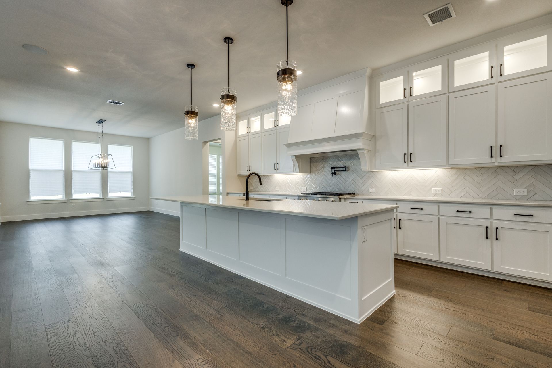 Modern white kitchen with island, pendant lights, and dark wood floors.