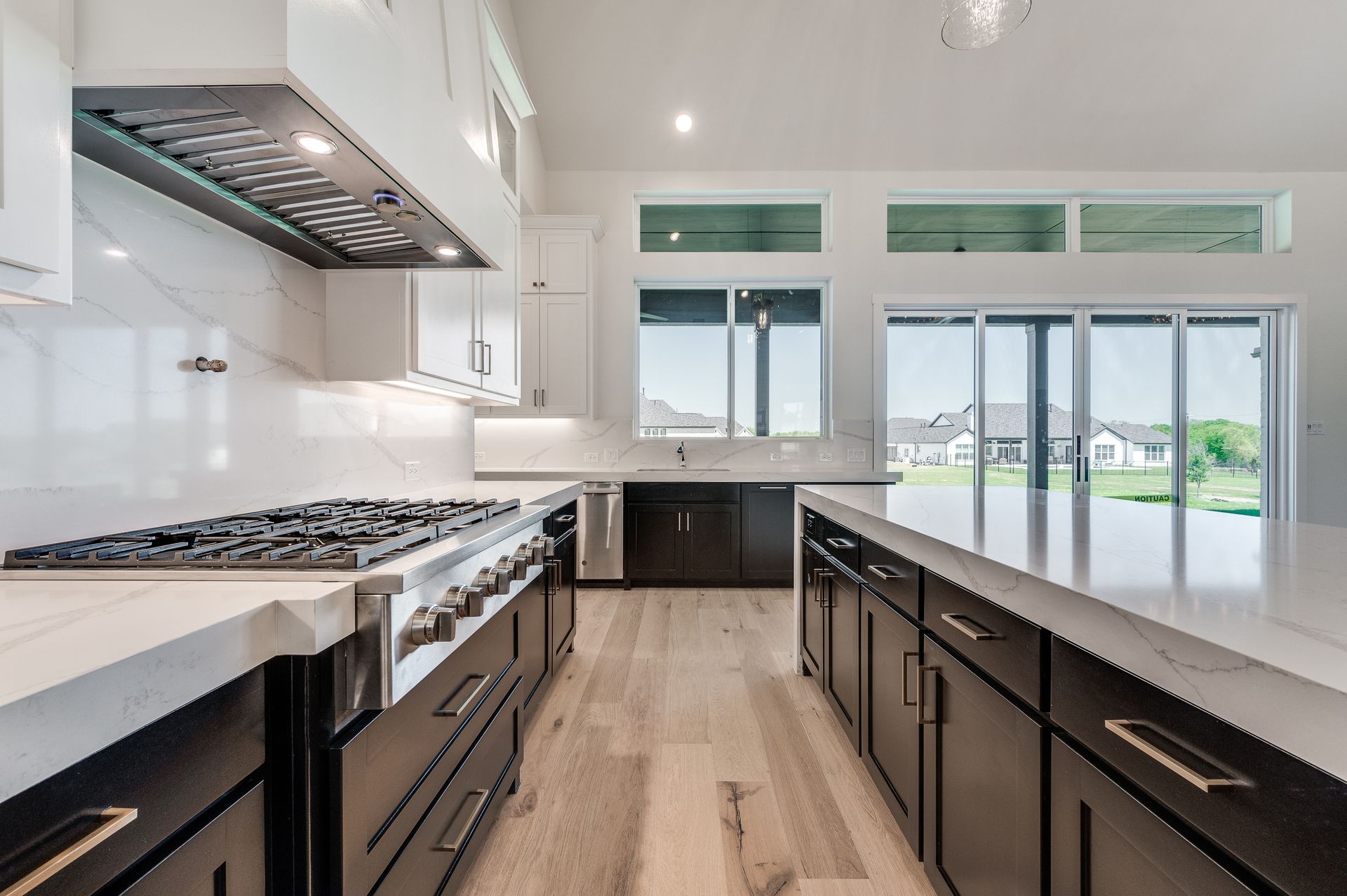 Modern kitchen with white countertops, dark cabinets, stainless steel appliances, and large windows.