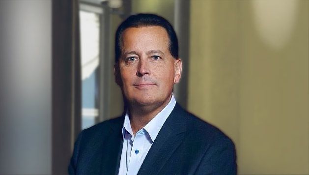 A man in a suit and white shirt is standing in a hallway.