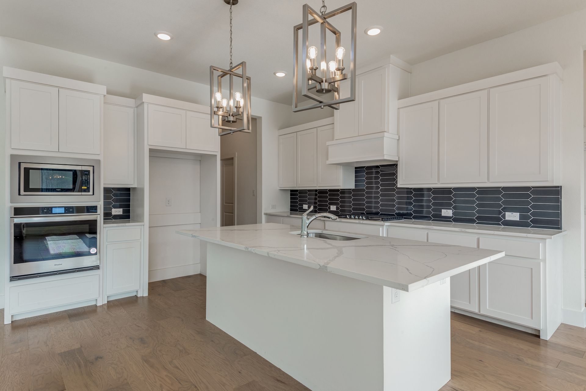 Modern white kitchen with island, cabinets, appliances, and light fixtures.