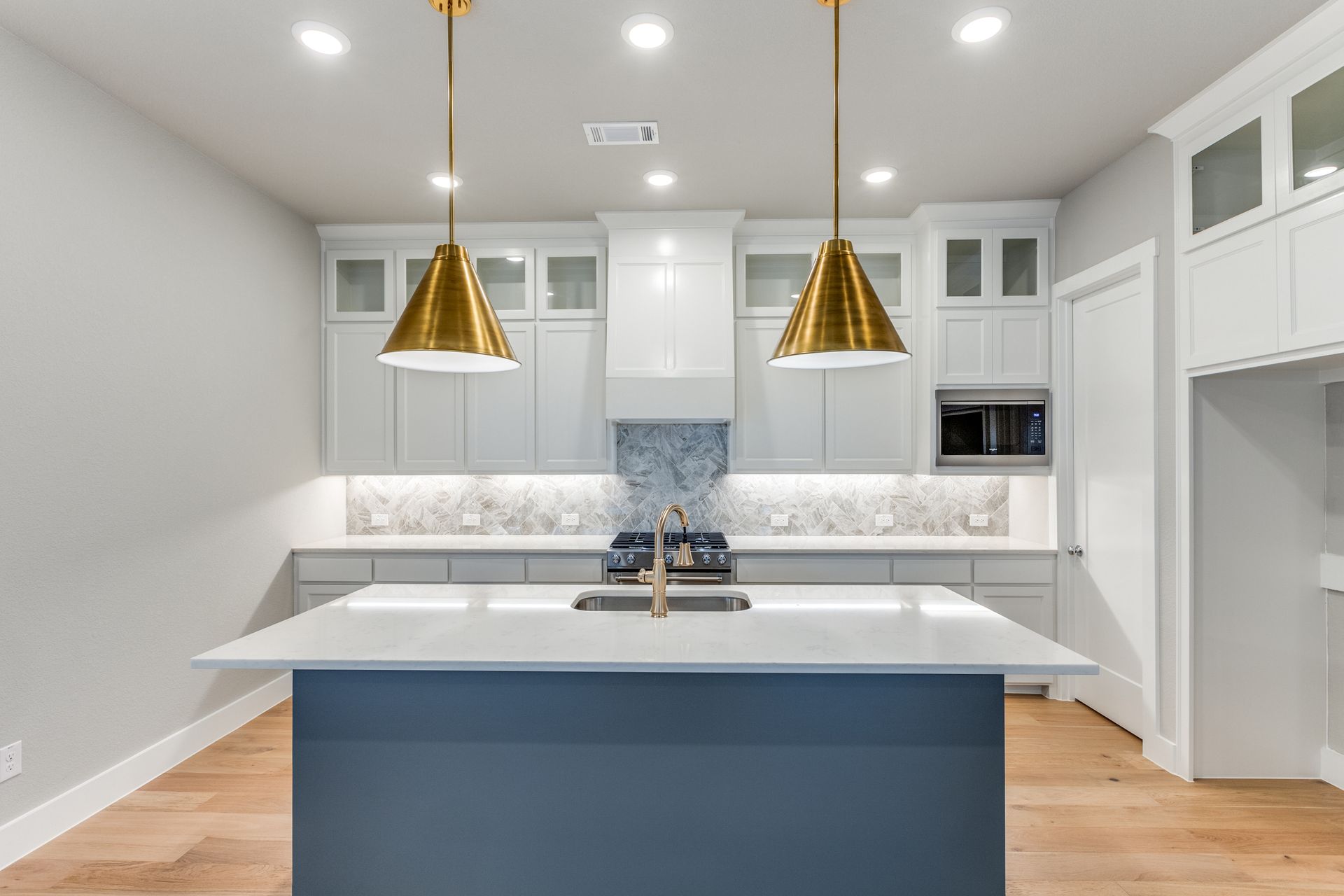 Modern kitchen with white cabinets, blue island, gold pendant lights, and wood floors.