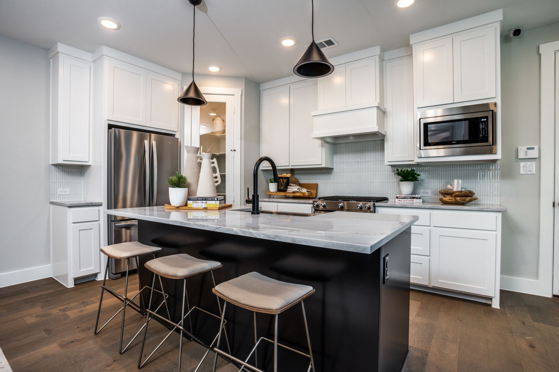 Modern kitchen with white cabinets, dark island, stainless steel appliances, and three bar stools.
