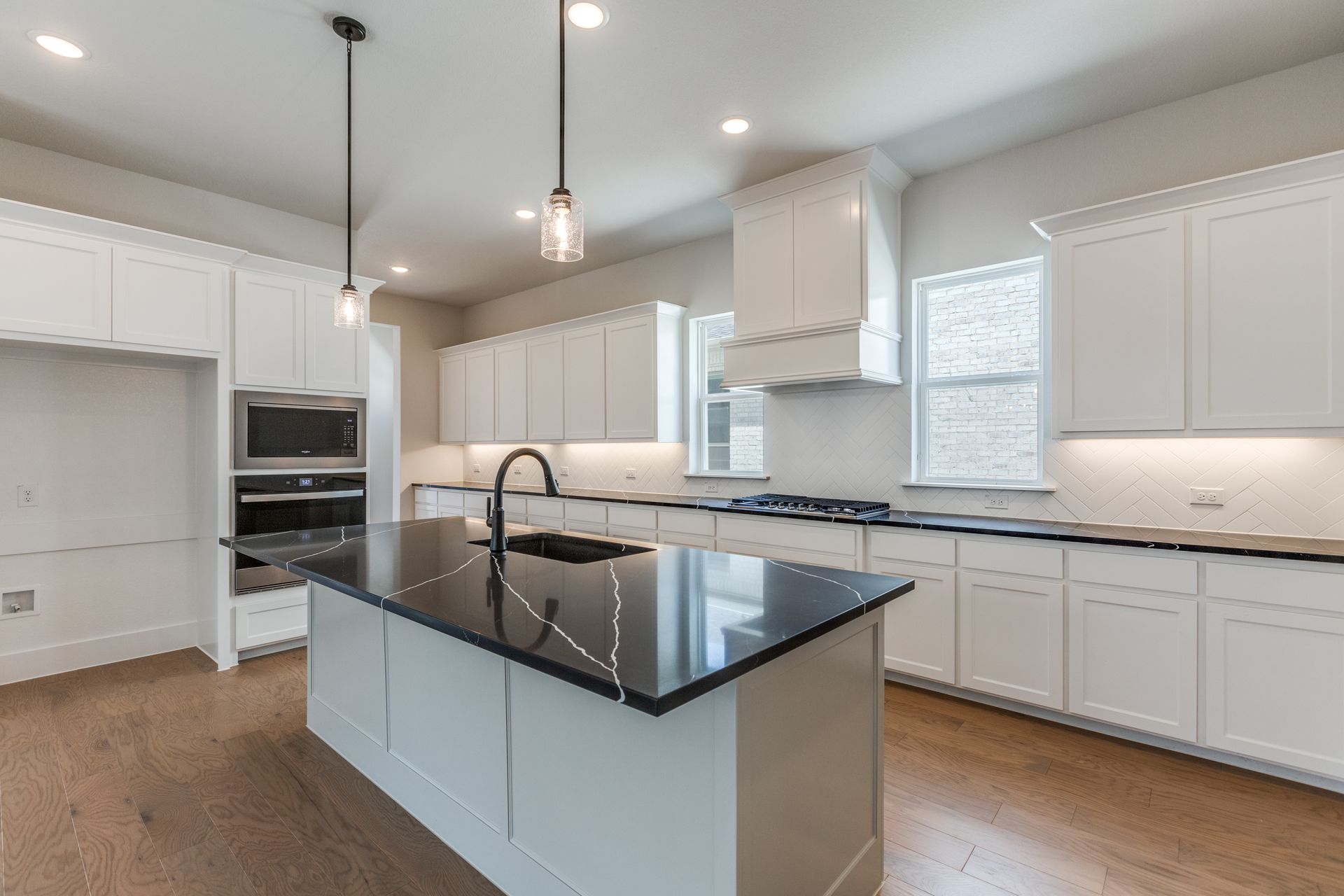 Modern white kitchen with black island, wood floor, and pendant lights.