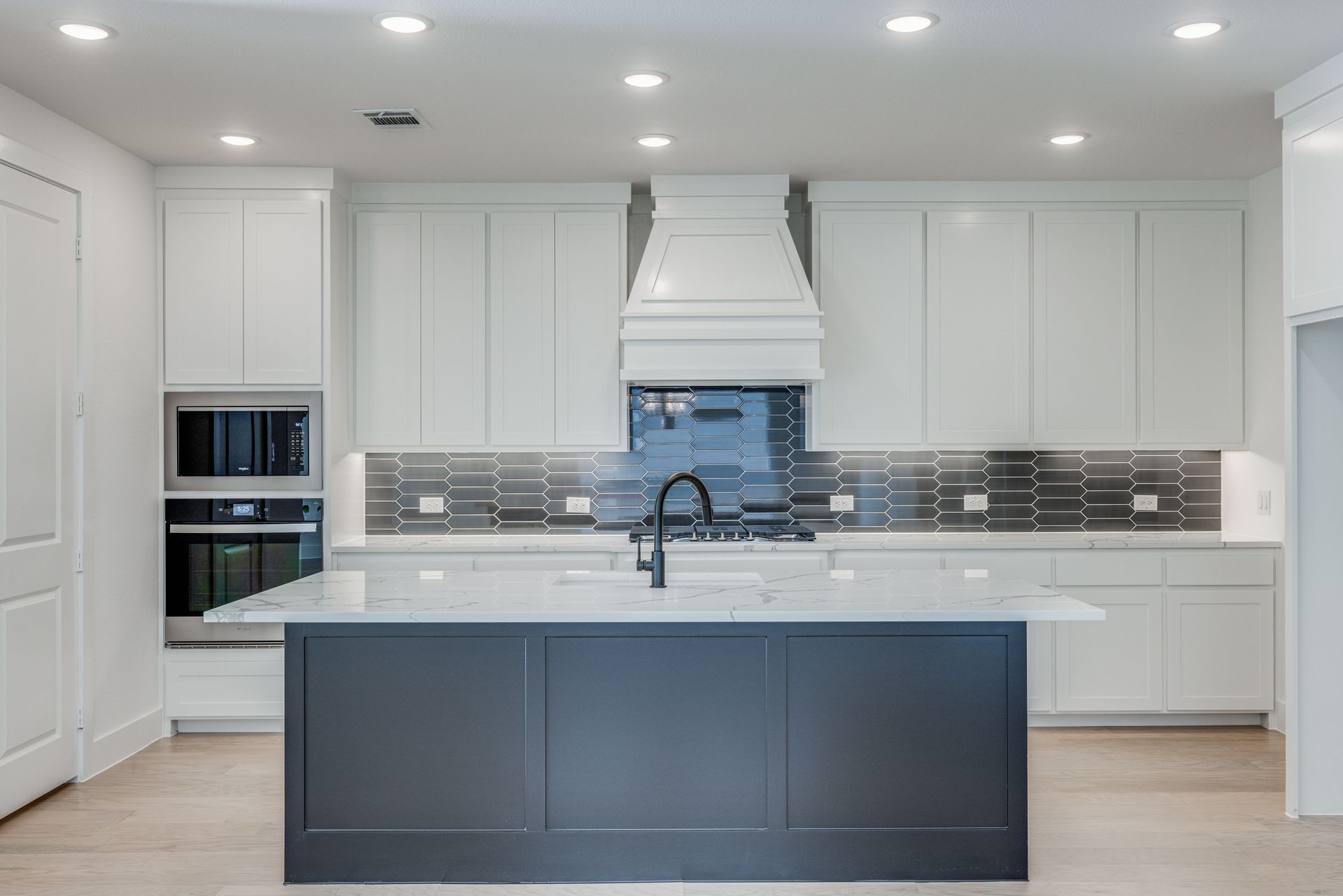 Modern white kitchen with navy island, stainless steel backsplash, and black faucet.